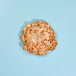Almond Croissant New York Cookie topped with toasted almond flakes on a light blue background from Crumbs & Doilies